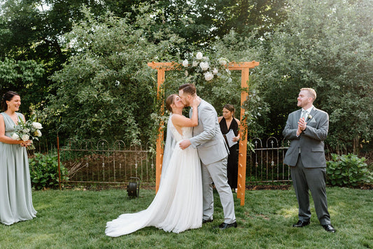 Bride and groom's first kiss under beautiful white flowers on wedding arbor